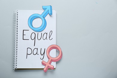 Photo of Equal pay. Open notebook and gender symbols on light grey background, top view with space for text
