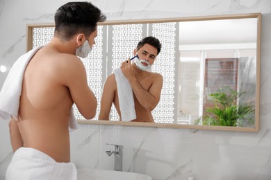 Handsome young man shaving with razor near mirror in bathroom, space for text