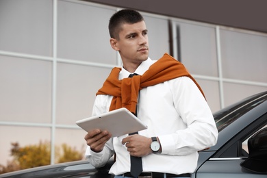 Attractive young man with tablet near luxury car outdoors
