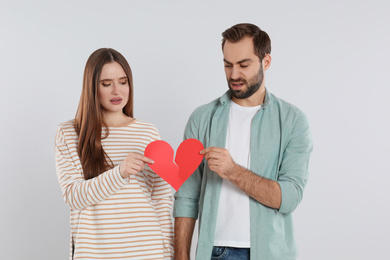 Couple tearing paper heart on light  background. Relationship problems