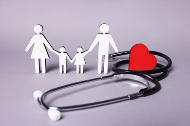 Photo of Figures of family stainding near stethoscope and heart on lilac background. Insurance concept