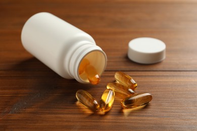 Overturned bottle with dietary supplement capsules on wooden table
