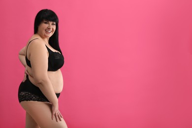 Beautiful overweight woman in black underwear on pink background, space for text. Plus-size model