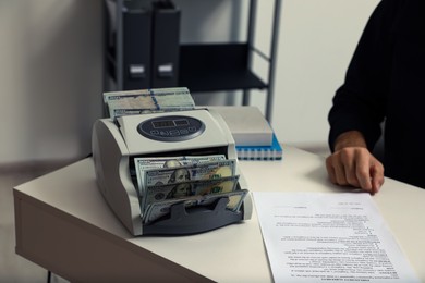 Photo of Man using banknote counter at white table indoors, closeup