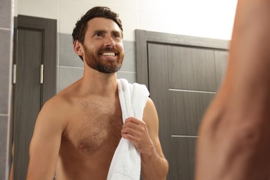 Handsome bearded man looking at mirror in bathroom near wooden doors