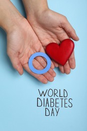 Woman holding blue paper circle and red heart near text World Diabetes Day on color background, top view