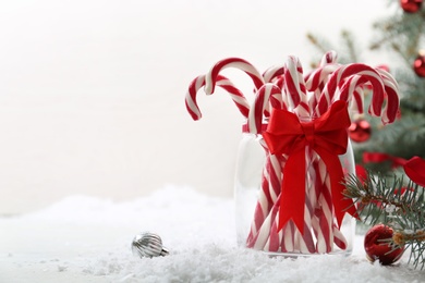 Candy canes in glass jar and Christmas balls on table against light background. Space for text