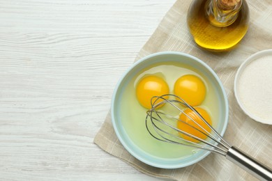 Whisking eggs in bowl on white wooden table, top view. Space for text