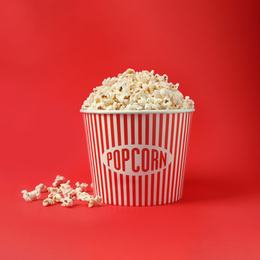 Delicious popcorn in paper bucket on red background