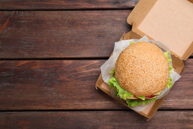 Delicious burger in cardboard box on wooden table, top view. Space for text