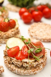 Crunchy buckwheat cakes with prosciutto, tomatoes and cucumber slice on white table, closeup