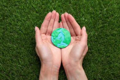 Happy Earth Day. Woman with plasticine planet on green grass, top view