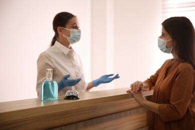 Receptionist with client at countertop in hotel, focus on dispenser bottle of antiseptic gel and service bell