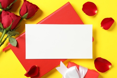 Flat lay composition with blank greeting card, notebook and roses on yellow background. Valentine's day celebration