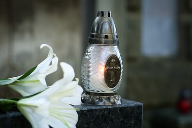 Lilies and grave lantern with burning candle on tombstone in cemetery, space for text