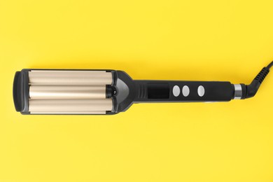 Modern triple curling iron on yellow background, top view