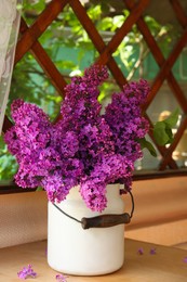 Beautiful lilac flowers in milk can on wooden table indoors