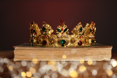 Beautiful golden crown, old book and fairy lights on brown background. Fantasy item