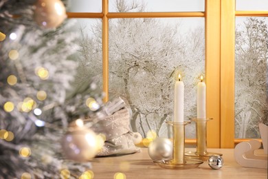 Burning candles and festive decor on window sill near Christmas tree indoors