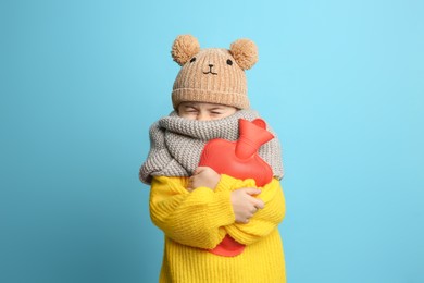 Ill girl with hot water bottle suffering from cold on light blue background