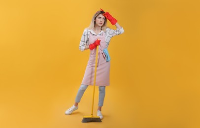 Young housewife with broom on yellow background