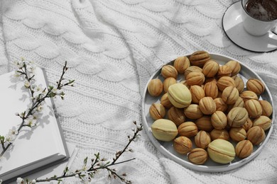 Photo of Delicious walnut shaped cookies with filling, cherry branches, notebook and cup of coffee on white knitted blanket, view from above and space for text. Homemade popular biscuits from childhood