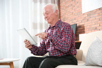 Elderly man using tablet PC on sofa in living room