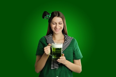 Image of Happy woman in St. Patrick's Day outfit with beer on green background