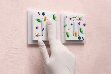 Image of Woman in protective gloves pressing light switch button full of microbes indoors, closeup