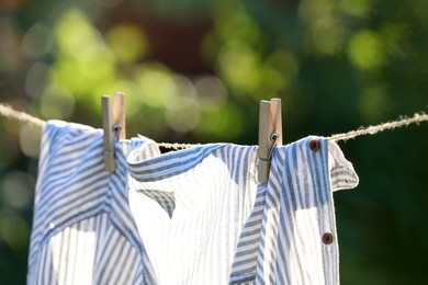 Washing line with drying shirt against blurred background, focus on clothespin