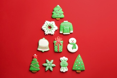Delicious gingerbread cookies arranged in shape of Christmas tree on red background, flat lay