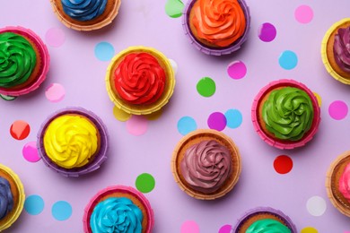 Many delicious colorful cupcakes and confetti on violet background, flat lay