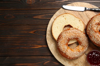 Delicious fresh bagels with sesame seeds and jam on wooden table, top view. Space for text