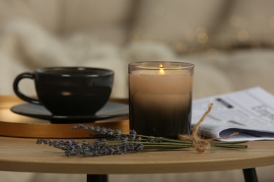 Photo of Beautiful candle, lavender, newspaper and cup on round wooden table in living room, closeup
