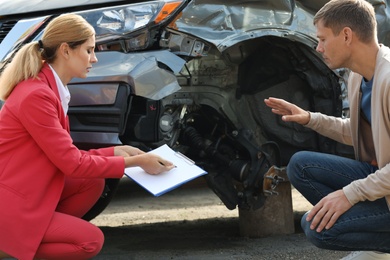 Man reporting and insurance agent filling claim form near broken car outdoors