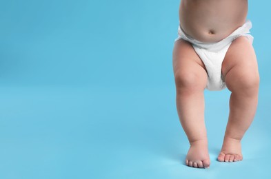 Cute baby in dry soft diaper standing on light blue background, closeup. Space for text