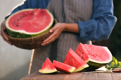 Woman holding wicker basket outdoors, closeup. Focus on delicious ripe watermelon slices with mint
