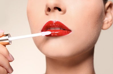 Beautiful woman applying red gloss on lips against color background, closeup
