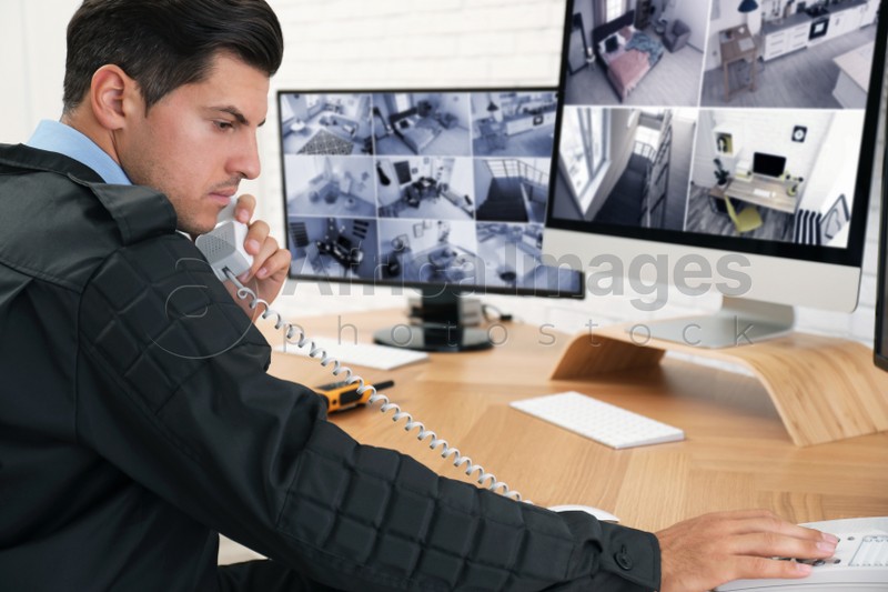 Photo of Male security guard talking by telephone near monitors at workplace