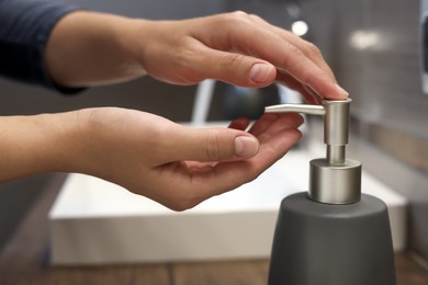 Woman using liquid soap dispenser in bathroom, closeup