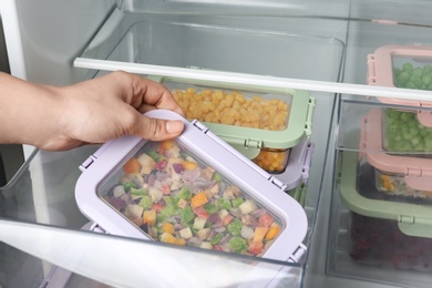 Photo of Woman taking box with vegetable mix from refrigerator, closeup