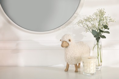 Photo of Burning soy candle, beautiful bouquet and decorative sheep on white table indoors. Space for text