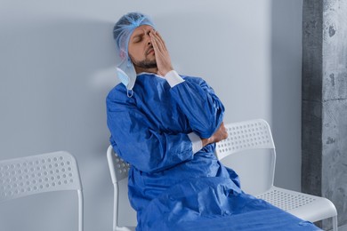 Exhausted doctor sitting on chair near grey wall indoors