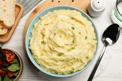 Bowl of tasty mashed potatoes with onion served on white wooden table, flat lay
