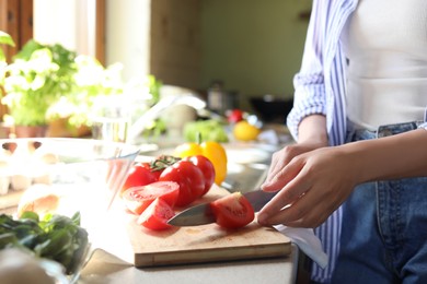 Woman cutting fresh tomatoes at countertop in kitchen, closeup