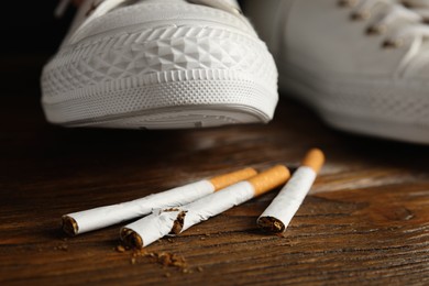 Photo of Woman stepping on pile of cigarettes, closeup. Quitting smoking concept
