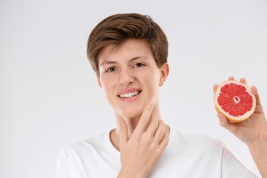 Teenage boy with acne problem holding grapefruit on light background. Skin allergy