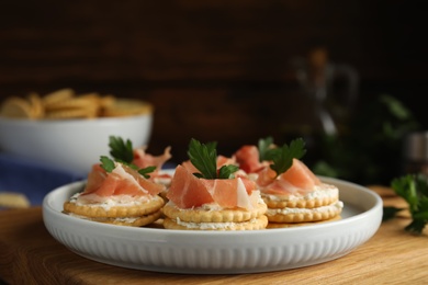Delicious crackers with cream cheese, prosciutto and parsley on table