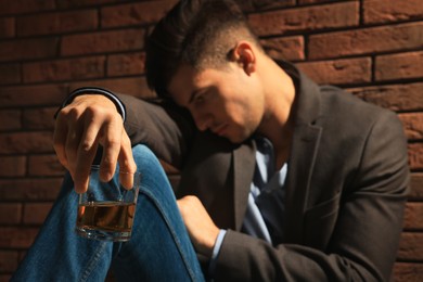 Addicted man near red brick wall, focus on glass of alcoholic drink