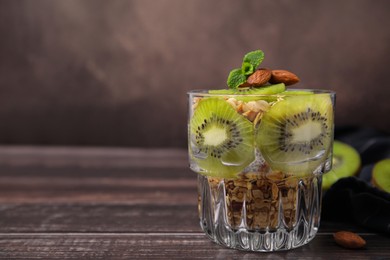 Photo of Delicious dessert with kiwi, muesli and almonds on wooden table, closeup. Space for text